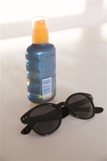 A bottle of suncream and a pair of black glasses on top of a table