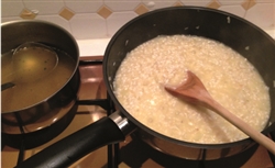 Image shows Spring onion, garlic, and prawn risotto before cooking. There are two pans - one containing chicken stock and one containing rice