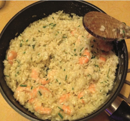 Image shows Spring onion, garlic, and prawn risotto in a pot after it has been cooked. The prawns can be seen mixed with the rice and other ingredients.