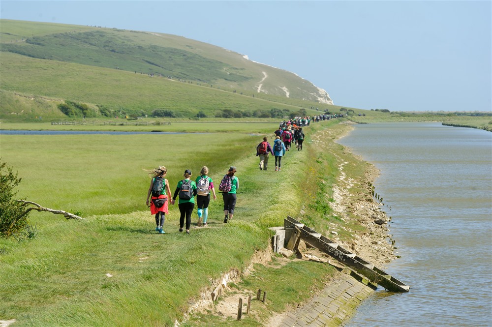 A group of people in a line waking through fields and the sea next to them