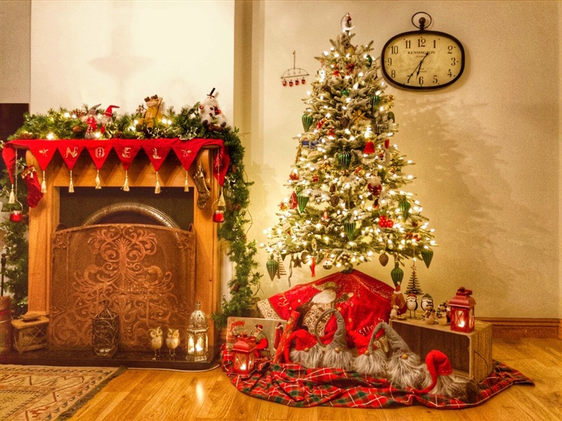 A cosy scene of a fireplace and a Christmas tree, decorated with twinkling lights and red and green ornaments.