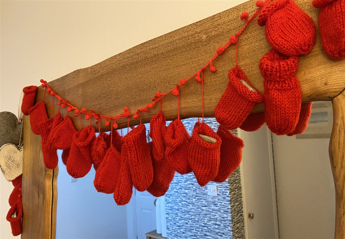 A knitted hanging decoration made of red wool and lots of mittens.