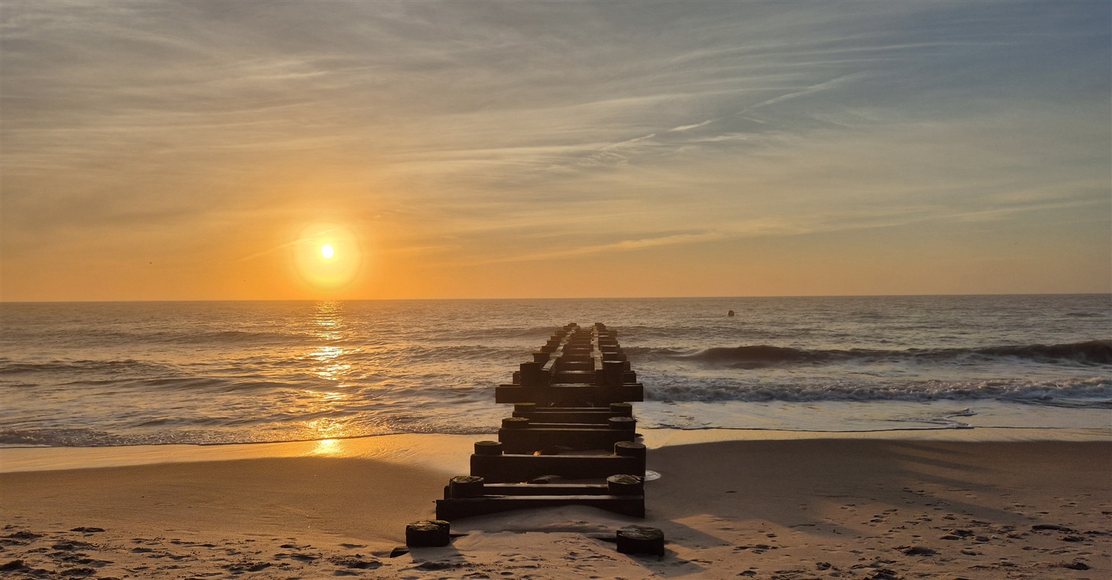 A beach at sunrise with an old pier in the centre.