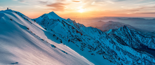 A snowy mountain against an orange sunrise
