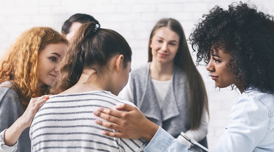 a group of people having a conversation and showing their support by placing a hand on someones shoulder