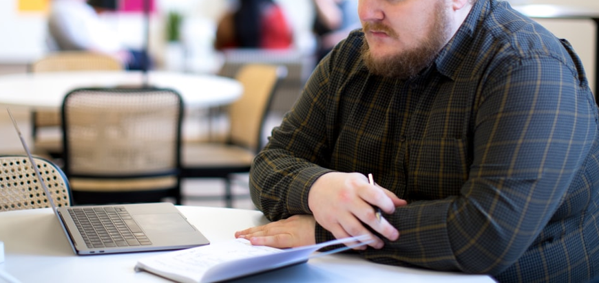 A person in a flannel shirt is looking at a laptop and some documents