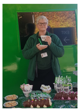 A picture of Alison in a Macmillan fleece having a cup of tea