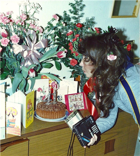  Photograph of Willo on her birthday, looking at a cake, cards and lots of blue and red flowers