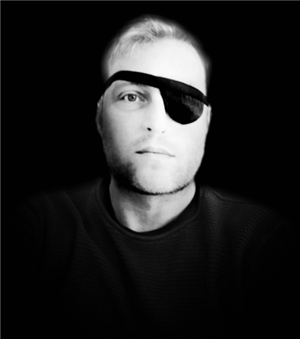 A black and white portrait image of Dan, wearing a patch over one eye.