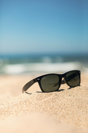  Sunglasses on sand with blue sky behind