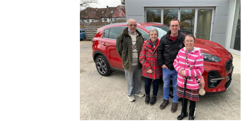  Amanda-Jayne with her husband Tristan, and parents in law, Sharron and David. They are all smiling, stood in-front of a red car.