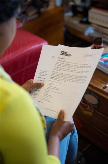 This images shows a woman reading a Macmillan fact sheet translated into Bengali.