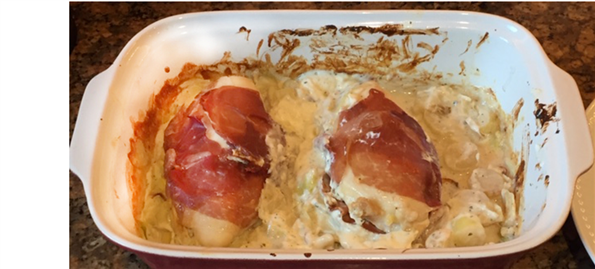 Picture of a white baking dish with two cooked chicken breasts and cheesy leaks around them