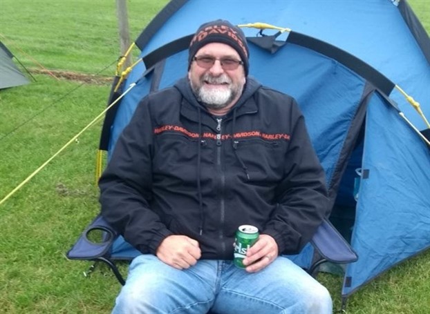  Man sat outside a blue tent in a field smiling at the camera