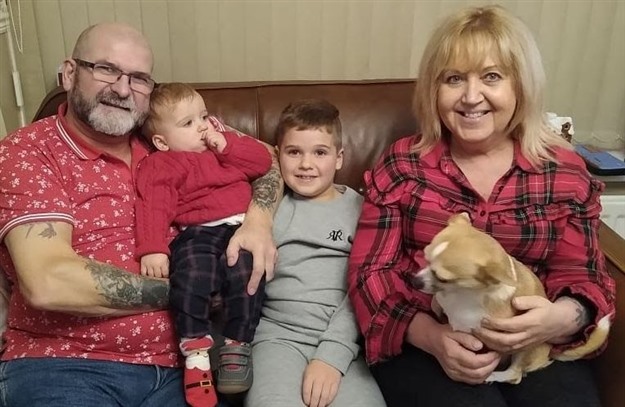 A photograph of Shaun and Janet with their two grandchildren and a dog, sat on a sofa and smiling