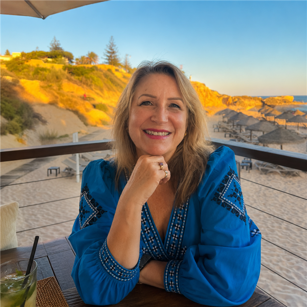 Fiona sits smiling on a balcony with sand dunes and beach huts visible in the background