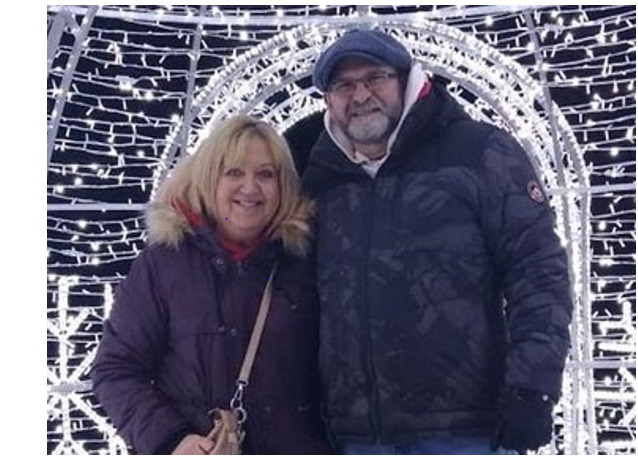  A photograph of a man and a woman, smiling at the camera with white Christmas lights in the background