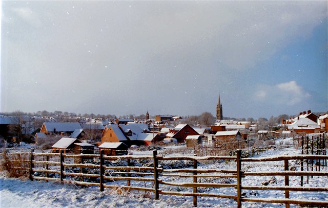 a snow covered village behind a traditional wooden fence with a church tower in the distance
