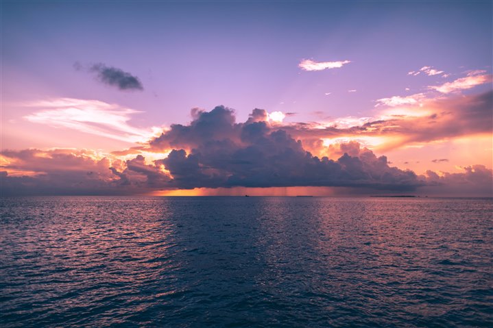  A pink and purple sky with clouds over a body of water.