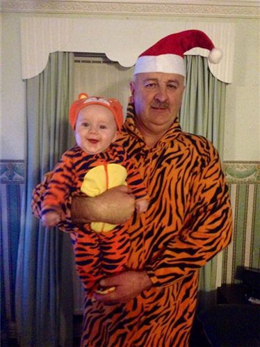 A man holding a baby, where both are in orange and black tiger costumes.