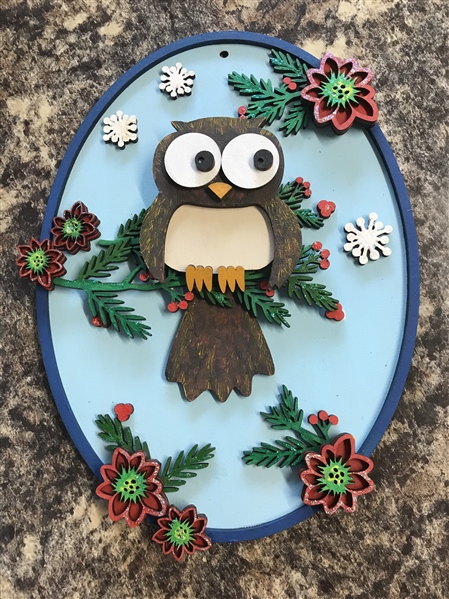 A handmade owl ornament fearing sprigs of holly and snowflakes.