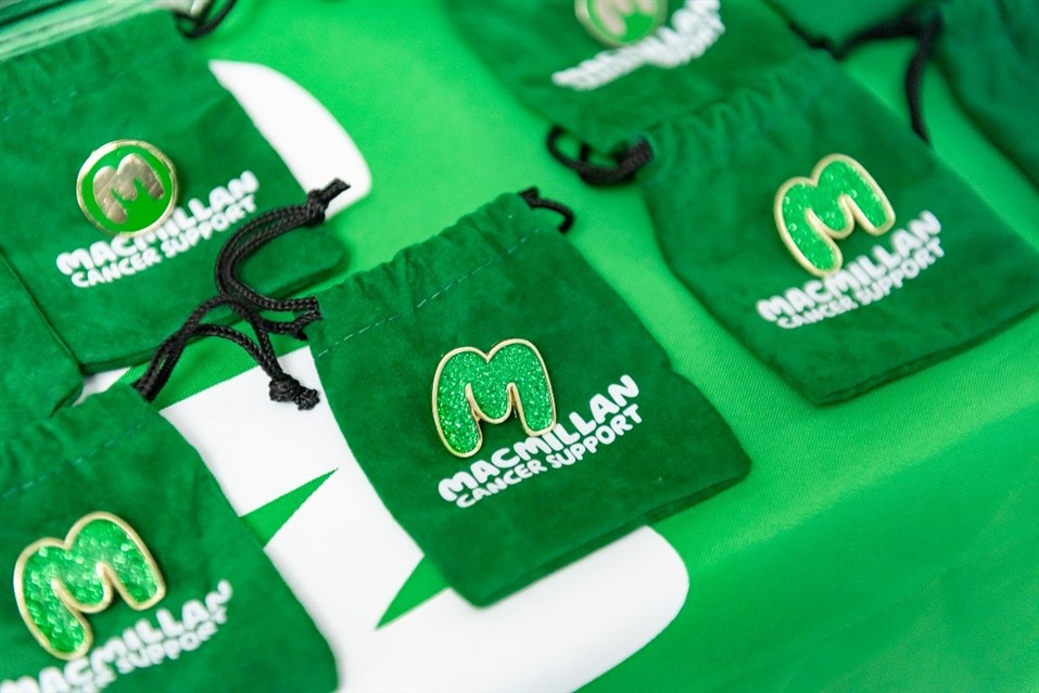 Photo of a row of Macmillan pin badges in the shape of an M on a table.