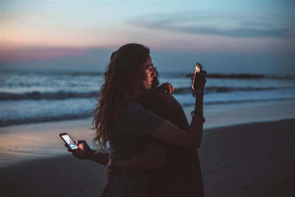 Two people hugging whilst looking at mobile phones