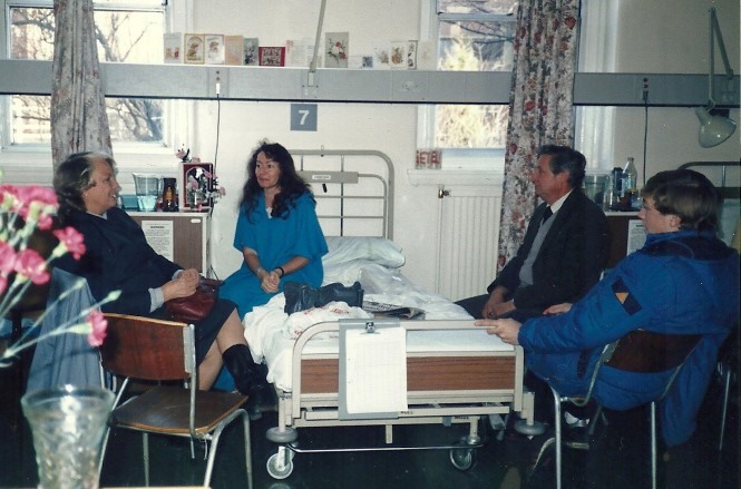  Photo of a Willo's Hospital room, Willo sits on her bed surrounded by 3 friends on chairs